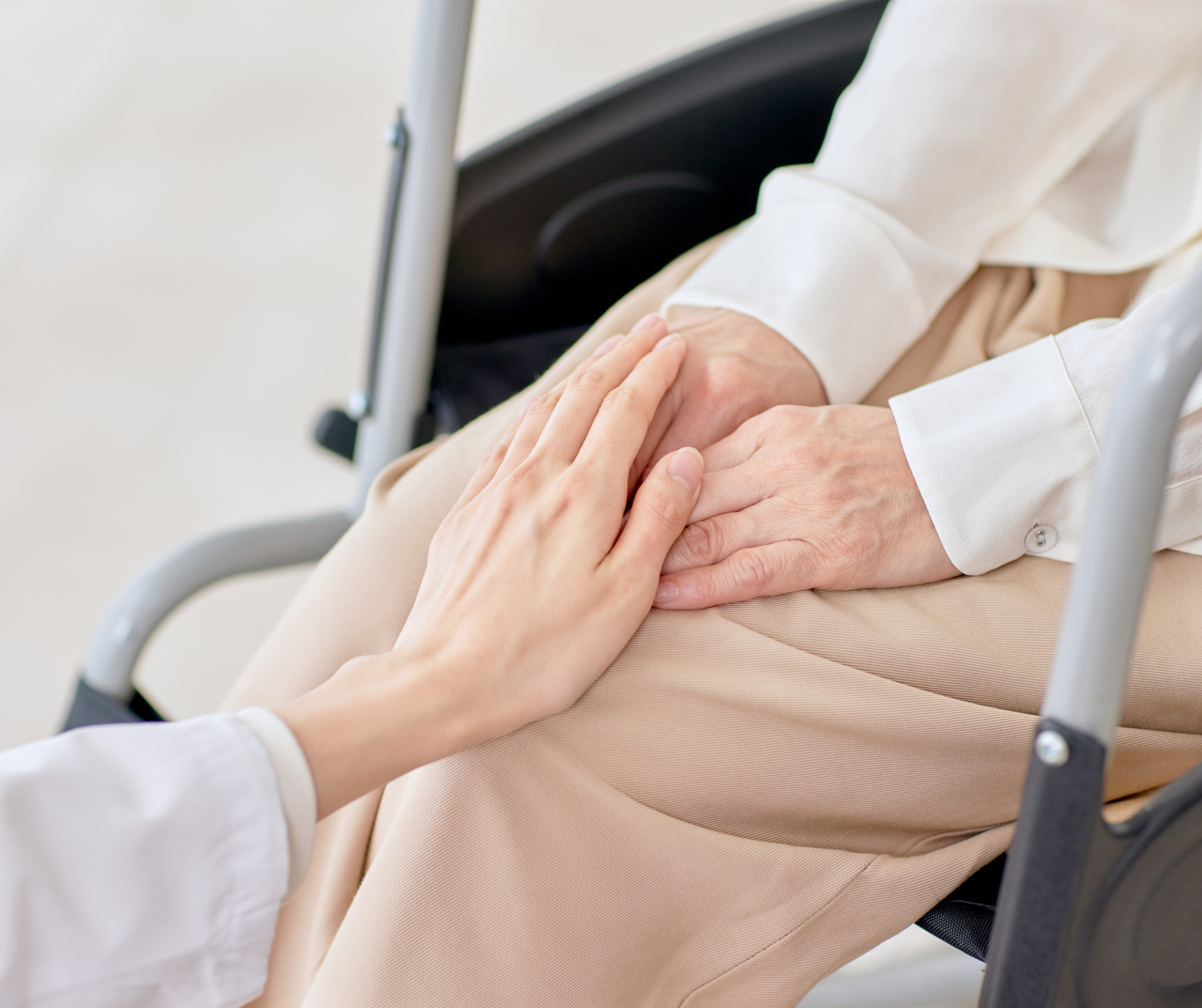 Caregiver holding the hand of an elderly person seated in a wheelchair.